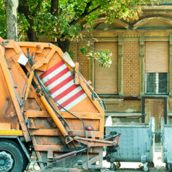 Rear end of garbage dumper truck near metal waste dumpster cans ready to collect litter. Public city cleaning.